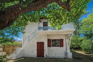 Um edifício de dois andares com varanda, porta de madeira e escadaria que leva ao andar superior.