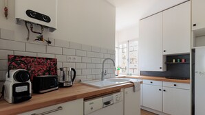 A modern kitchen with white cabinets, a wooden countertop, a built-in dishwasher, and a coffee maker. - Appartement Prunelle - Welkeys (Soorts-Hossegor)