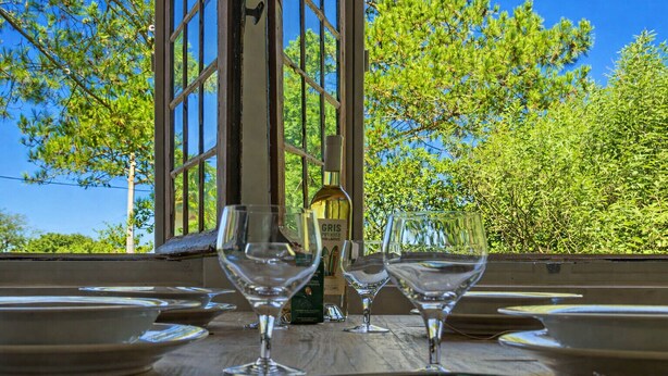 A table with wine glasses and a bottle, set against a backdrop of trees and a clear sky. - Appartement Prunelle - Welkeys (Soorts-Hossegor)