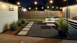 Un jardin avec un espace patio, des sièges d’extérieur et des guirlandes lumineuses.