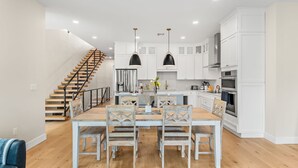 A modern kitchen with white cabinets, a wooden dining table, and a staircase.