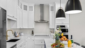 A modern kitchen with white cabinetry, stainless steel appliances, and a breakfast setup on the island.