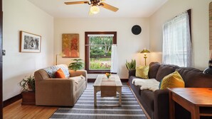 A living room with a sofa, a coffee table, a ceiling fan, a window with a view of greenery, and a lamp. - Charming 2-bedroom house in Viroqua with AC (Viroqua)
