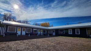 Un motel amb una fila de habitacions, una zona de pàrquing coberta i un camí d'accés de grava.