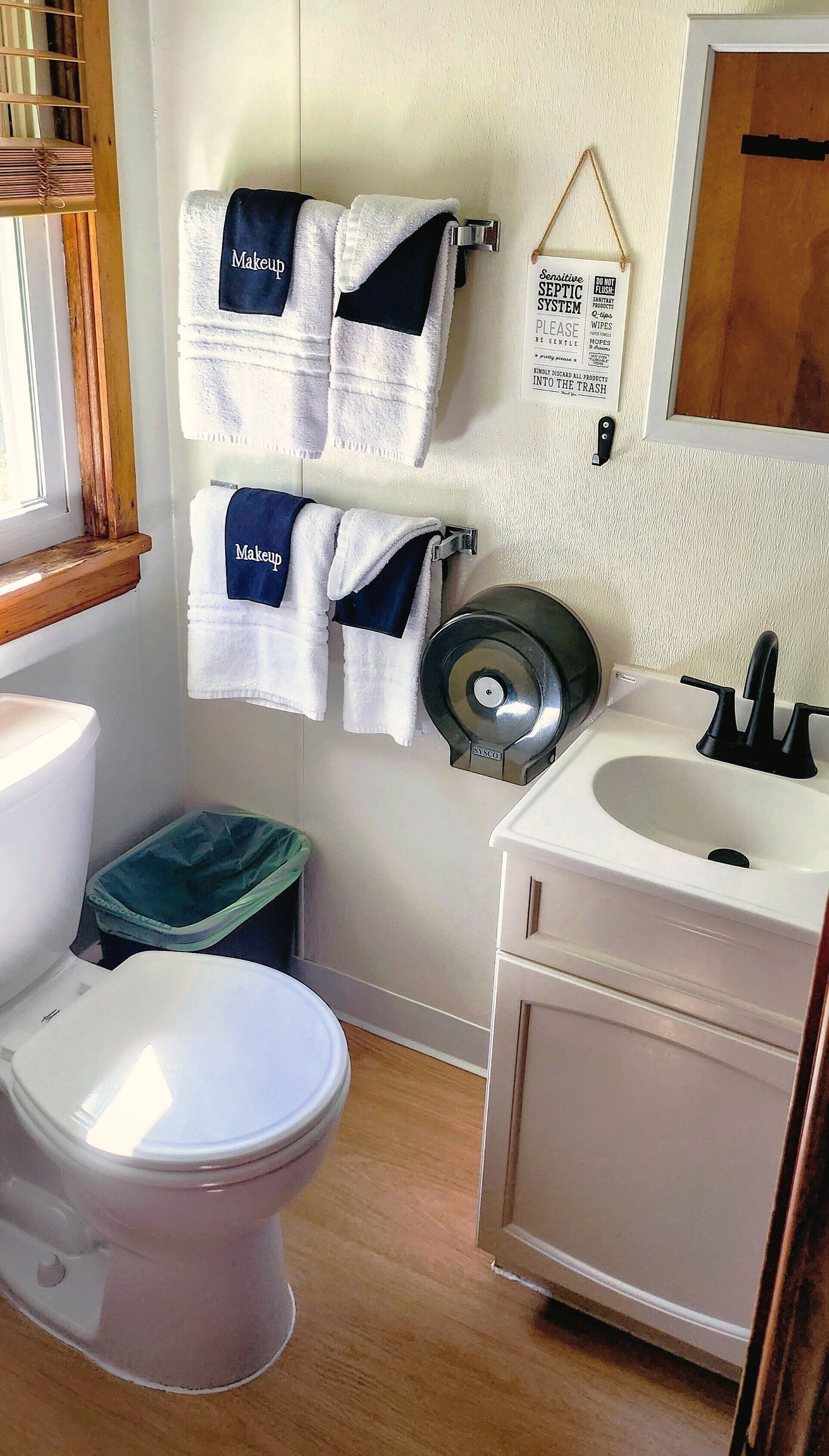 Un baño con inodoro, lavamanos y dos toallas colgando en la pared, etiquetadas como "Maquillaje".