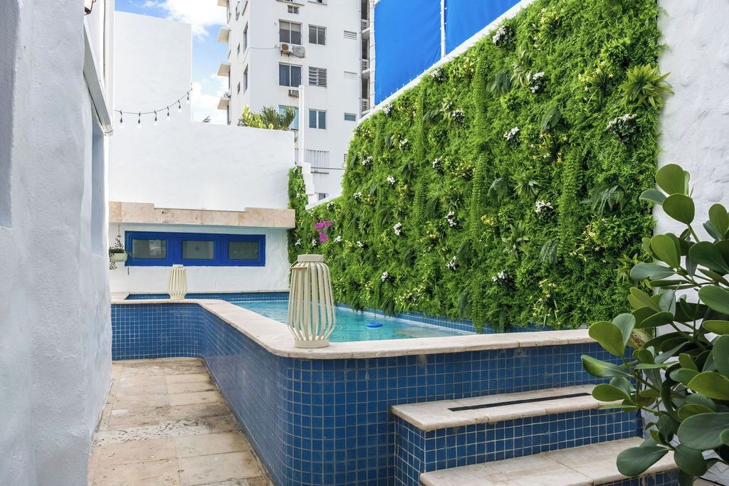 Un espace piscine avec des carreaux bleus, un mur blanc et un jardin vertical verdoyant.
