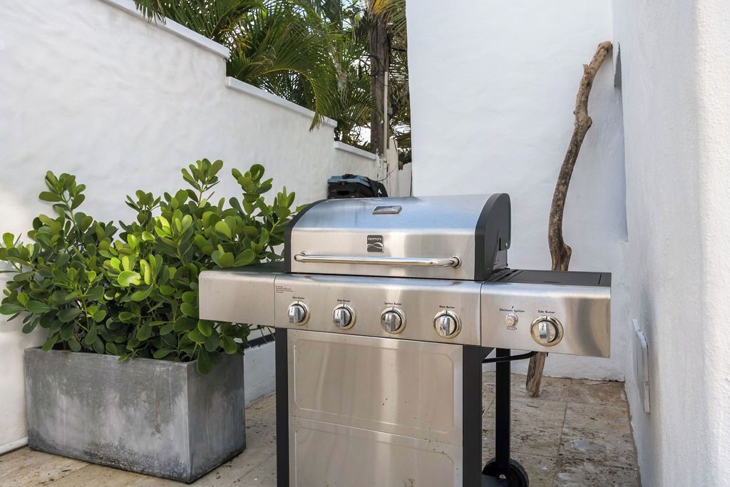 Un barbecue en acier inoxydable doté de quatre brûleurs et d’un brûleur latéral, installé à l’extérieur, à côté d’un bac à fleurs en béton orné de feuillage verdoyant.