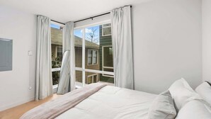 A bedroom with a large bed, a window with curtains, and a view of a house outside.