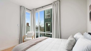 A bedroom with a large bed, a chair, and a window with curtains.