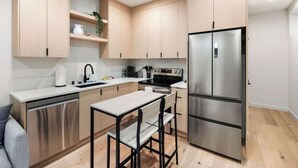 A modern kitchen with light wood cabinets, stainless steel appliances, and a central island with seating.
