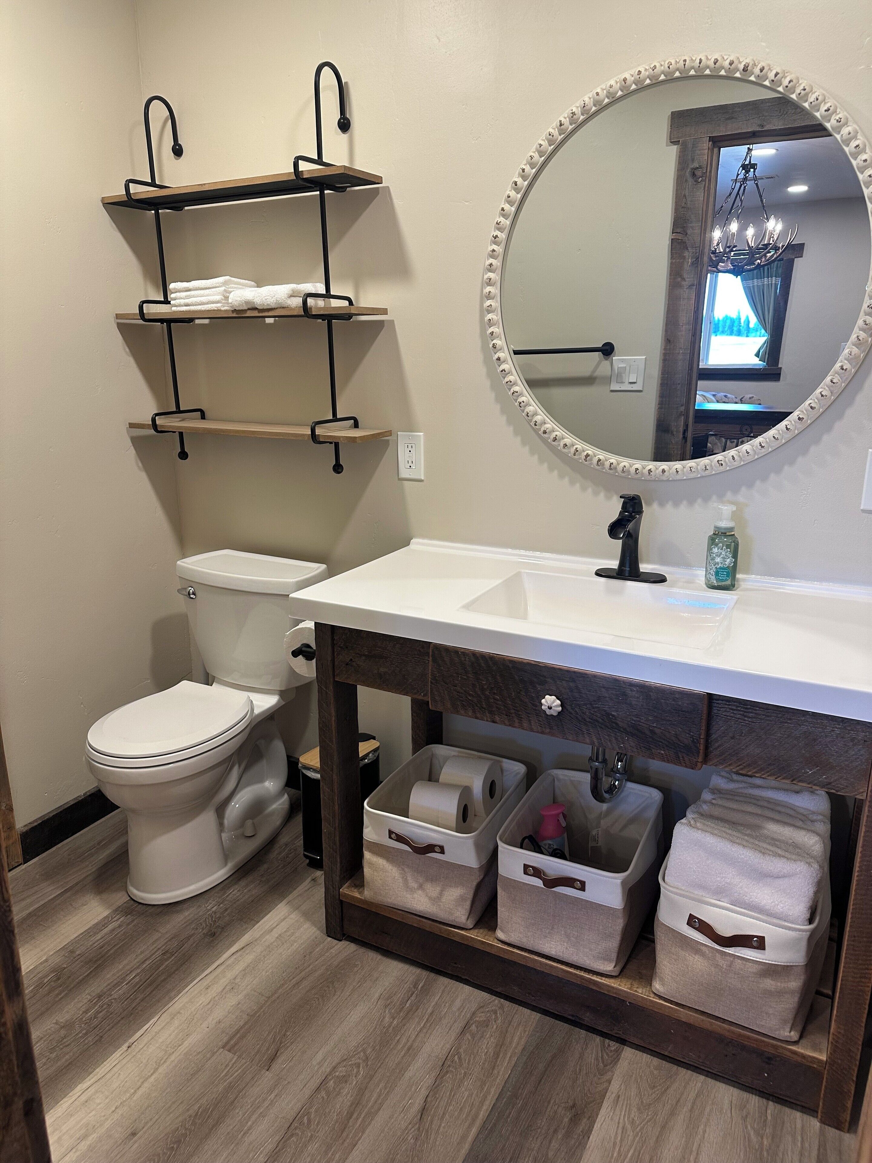 A bathroom with a white toilet, a sink with a mirror above it, and shelves above the toilet.