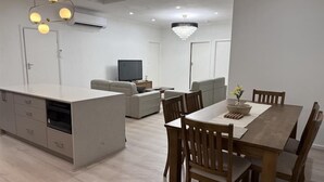 Cozinha moderna com ilha central, mesa de jantar com cadeiras e área de estar com sofá e televisão.