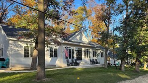 Une maison blanche avec un porche, un drapeau et des sièges à l’extérieur.