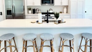 Une cuisine moderne avec des meubles blancs, un réfrigérateur en acier inoxydable, un four à micro-ondes et un grand îlot central doté de tabourets de bar.