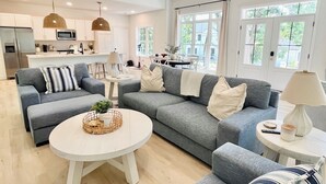 Un salon spacieux avec un canapé gris, une table basse ronde et une cuisine en arrière-plan.