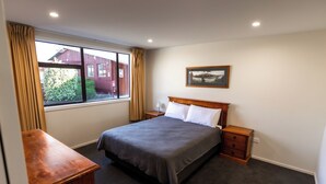 Ein ordentlich eingerichtetes Schlafzimmer mit Bett, Nachttischen, einem Schreibtisch und einem Fenster mit Vorhängen.