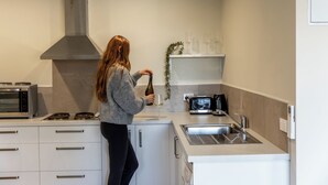 Eine moderne Küche mit weißen Schränken, einer Edelstahl-Dunstabzugshaube, einem Einbauofen, einer Kaffeemaschine und einem Spülbecken.