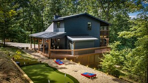 A cabin with a deck, surrounded by trees and a small pool. - Cavalier Cabin - Pet Friendly | Hot Tub | Mountain View | Game Room (Blue Ridge)