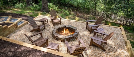 Un foyer entouré de fauteuils Adirondack en bois, situé dans une zone boisée.