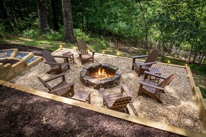 A fire pit surrounded by wooden Adirondack chairs in a forested area.