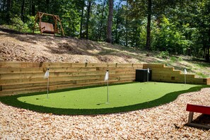 A playground with a wooden swing set, a green artificial turf area with flags, and a wooden bench.