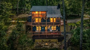A two-story cabin with a deck, surrounded by forest.