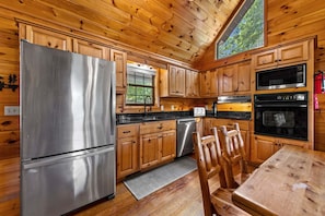 A cabin-style kitchen with wooden cabinets, a stainless steel refrigerator, a dishwasher, and a stove.
