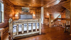 A wooden cabin bedroom with a bed, a painting, and a staircase.