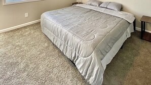 A bedroom with a large bed, a window, and a ceiling vent.