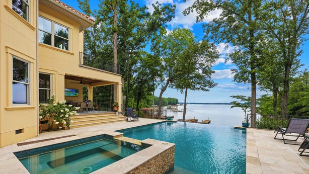Una casa de dos pisos con piscina, mobiliario exterior y vista a un lago.