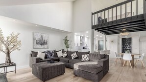 A modern living room with a sectional sofa, a dining area, and a staircase.