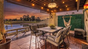 An outdoor patio with a table and chairs, a hanging chair, a potted plant, and a view of a body of water and greenery.