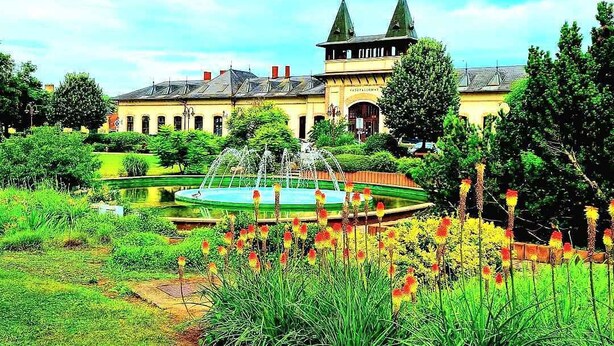 A large building with a fountain in the center, surrounded by well-maintained gardens and trees.
