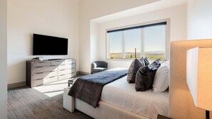 Ein modernes Schlafzimmer mit Bett, Kommode, Fernseher und Fenster mit Blick.