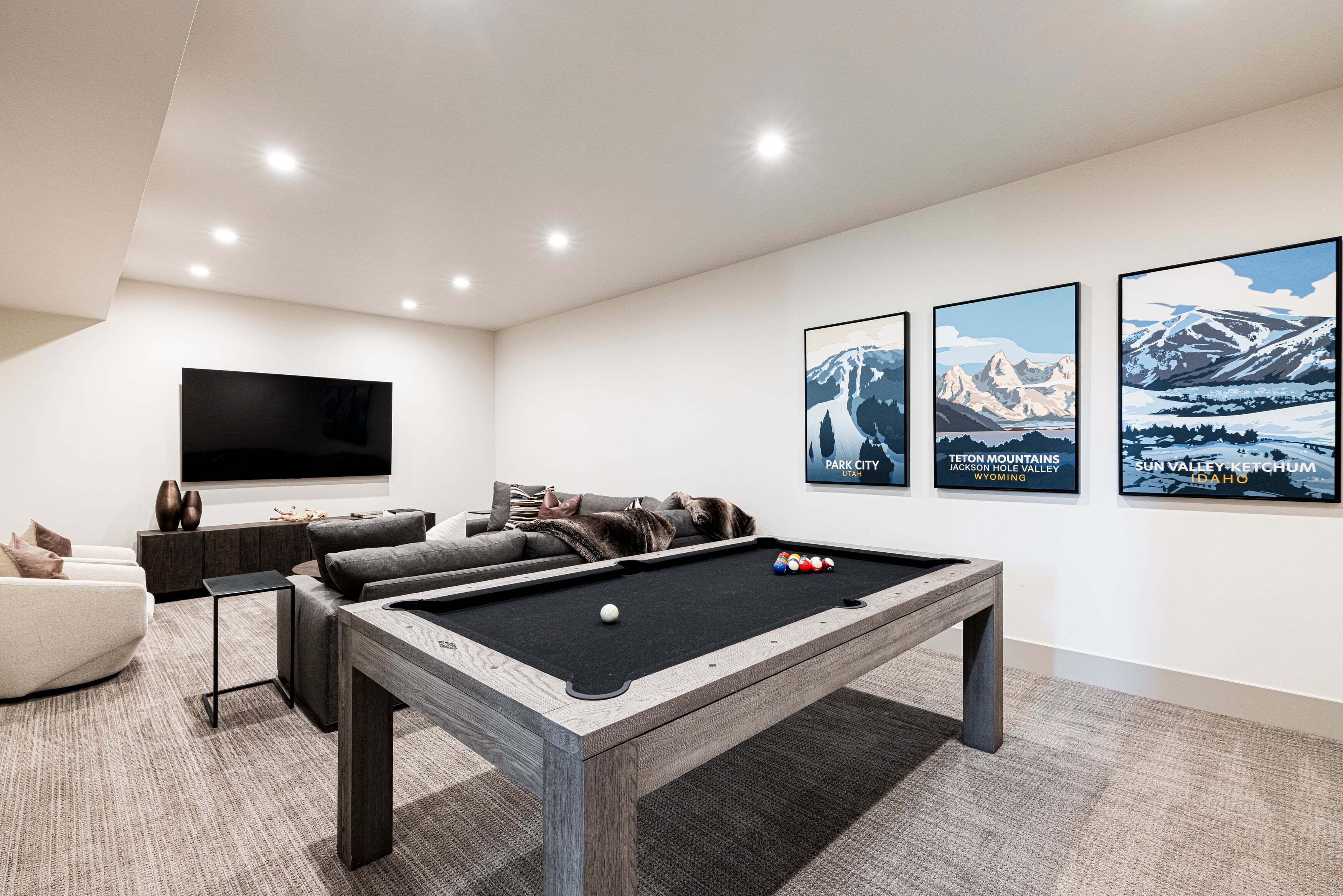 A modern living room with a pool table, a flat-screen TV, a sofa, and three framed landscape posters.