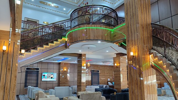 Eine prächtige Hotelhalle mit einer geschwungenen Treppe, komfortabler Sitzgelegenheiten und einem großen Bildschirm.