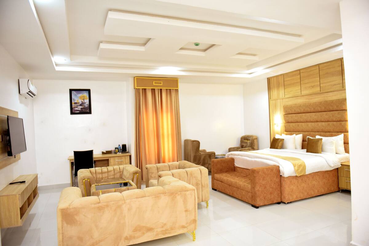 A modern hotel room with a large bed, a sofa, a desk, and a TV.