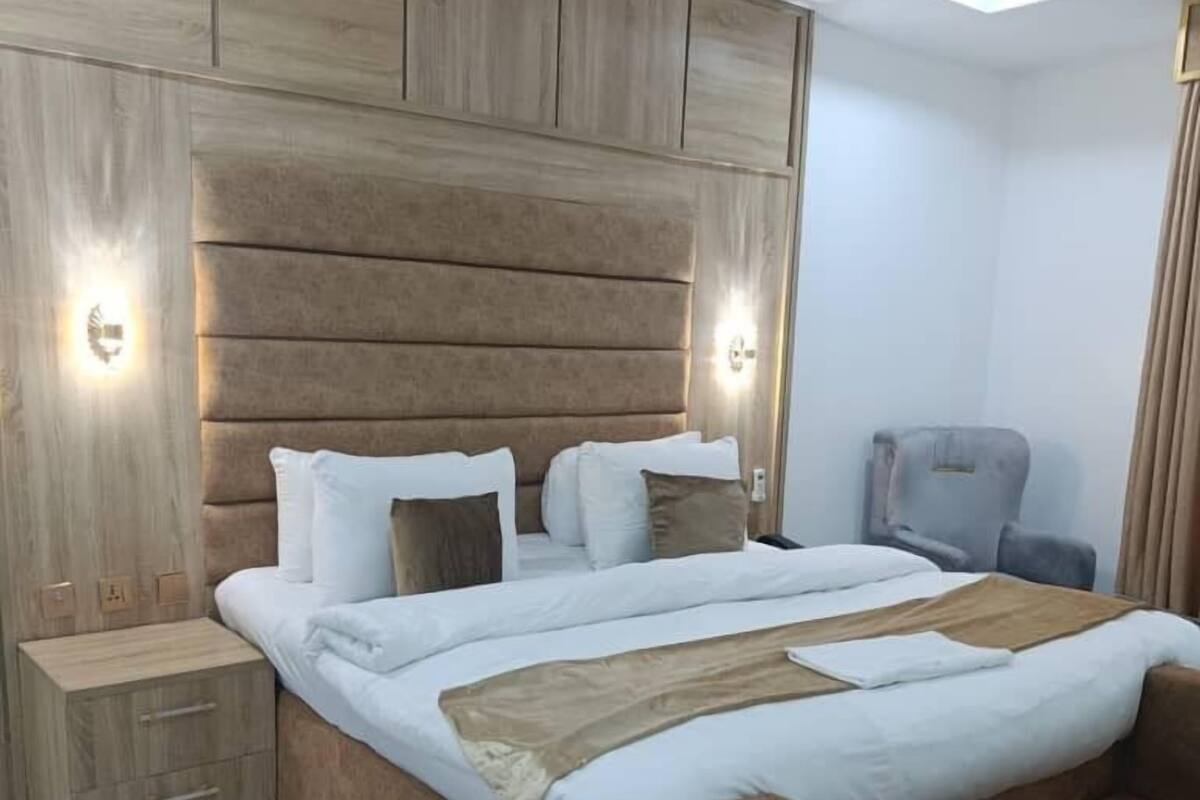 A modern bedroom with a large bed, wooden headboard, bedside tables, and a chair.