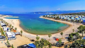 A coastal area with a beach, parked vehicles, and a row of blue buildings. - Mobile Home in Omisalj by Pusca Bay Beach (Omisalj)