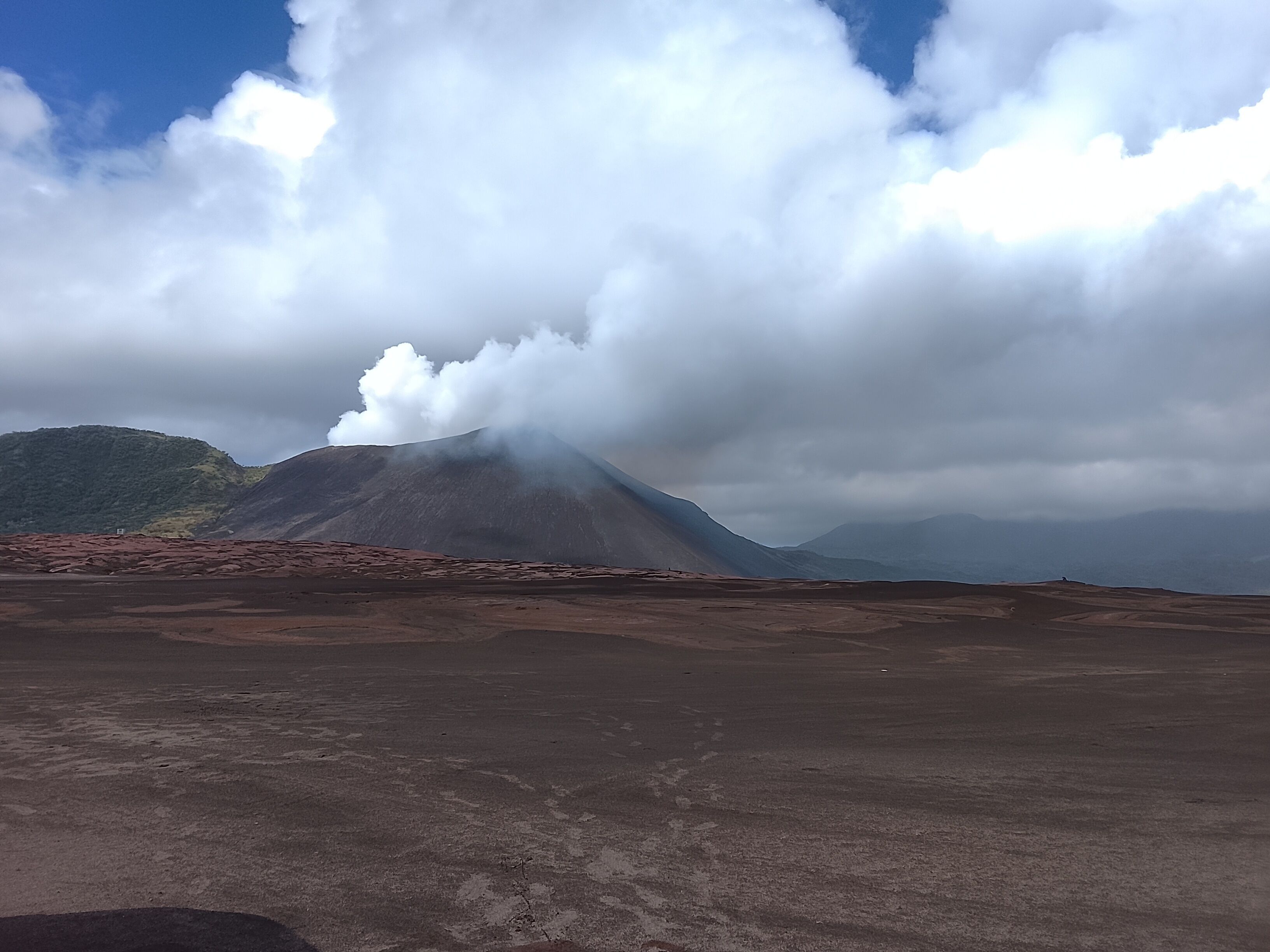 A barren landscape with a mountain in the background and clouds above.