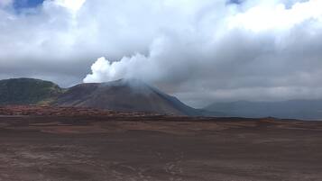 A barren landscape with a mountain in the background and clouds above.