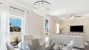 Un salon moderne avec une table à manger en verre, des sièges confortables, un ventilateur de plafond et un téléviseur.