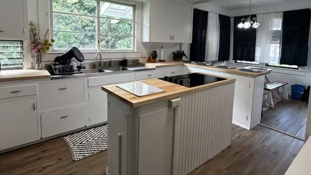 Een moderne keuken met witte kastjes, een centraal eiland en een groot raam voor natuurlijk licht.