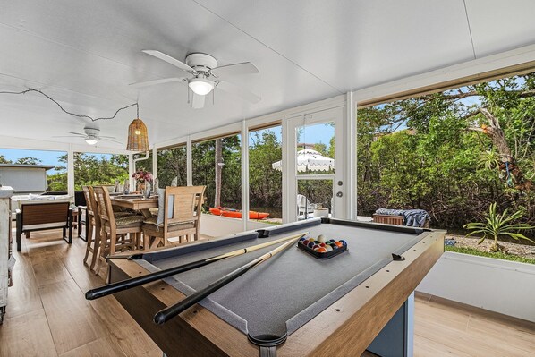 A pool table with pool cues and balls, a ceiling fan, and a dining area with chairs and a table.