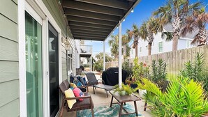 An outdoor patio with a covered seating area, a grill, and potted plants.