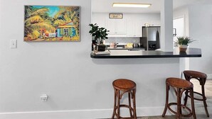 A kitchen with a bar area, a painting, and a sign that reads "BEACH HOUSE".
