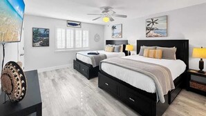 A bedroom with two beds, a ceiling fan, and artwork on the walls.
