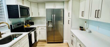 A modern kitchen with white cabinets, a stainless steel refrigerator, and a microwave.