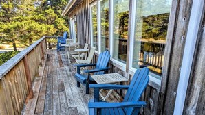 Une terrasse en bois avec des chaises Adirondack bleues et une petite table, donnant sur une zone boisée.