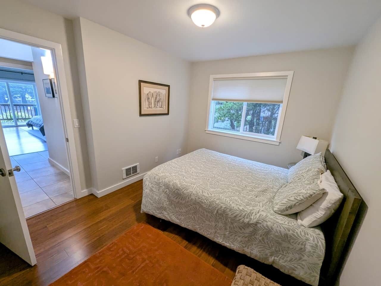 A bedroom with a bed, a window, a door, and a framed picture on the wall.